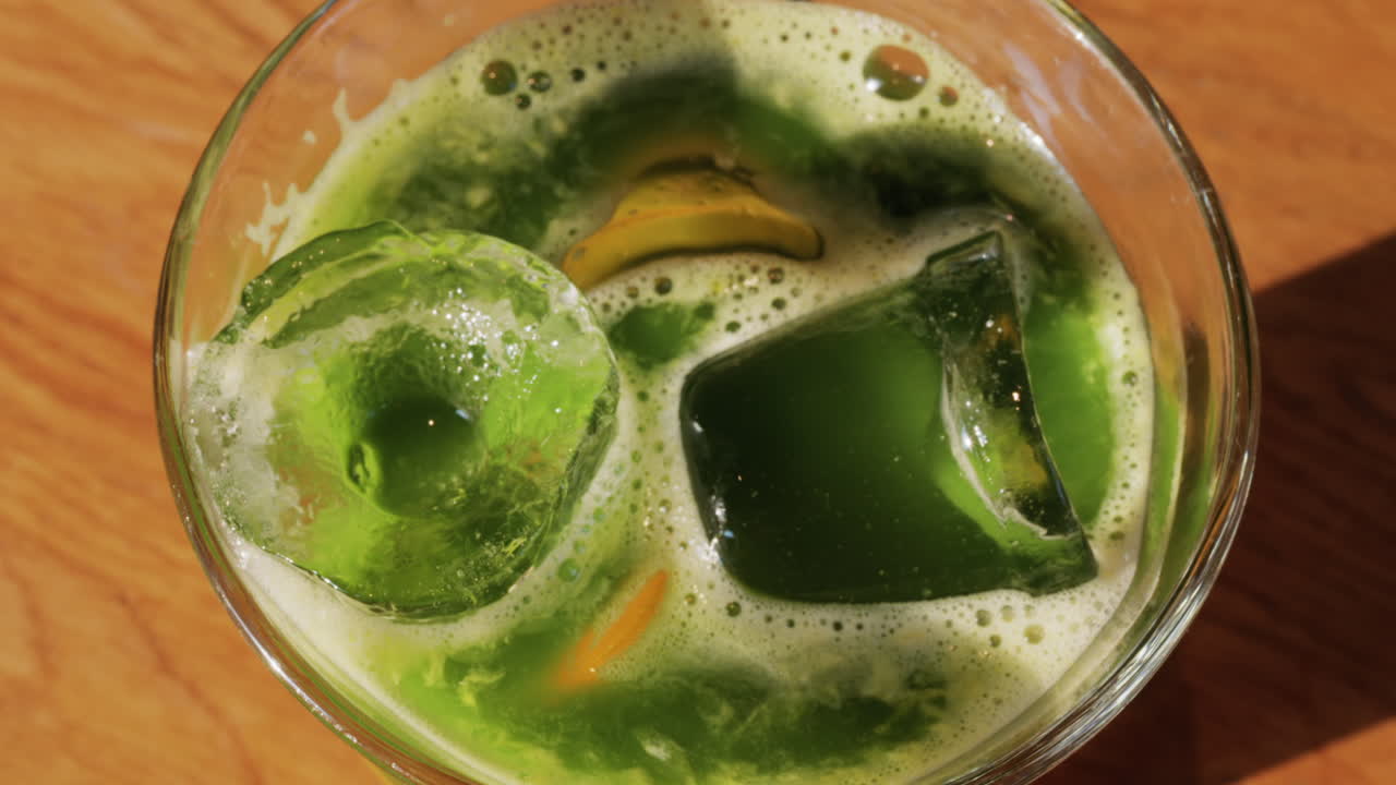 Close up of a glass of an iced orange juice matcha on a table at a cafe