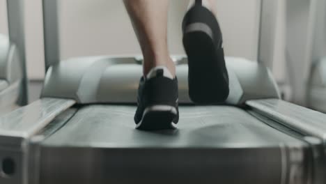 pies de primer plano comenzando a correr en la cinta de correr en el gimnasio de fitness. vista posterior de los zapatos negros