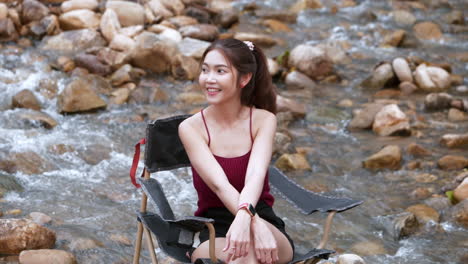 asian woman in red sitting on a chair with big rocks and water slow splashing for relaxing and happiness in the vacation summertime