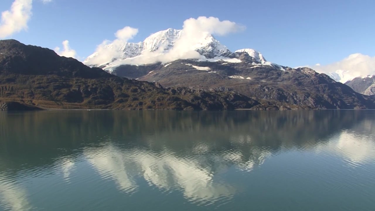 Giornata di sole a Glacier Bay, Alaska. Nuvola bianca sulla cima della montagna innevata. Riflesso della montagna innevata nell'acqua