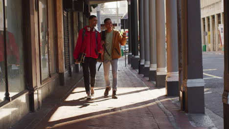 two happy biracial male friends walking and talking in the street