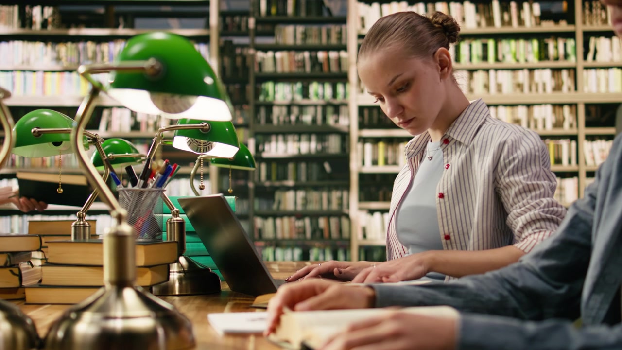 Giovane studentessa che lavora al portatile al tavolo di legno della biblioteca.