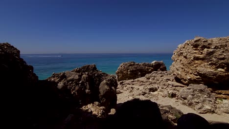 costa rocosa en el mar azul turquesa del mediterráneo, jet ski en el horizonte visto a través de acantilados en la playa tranquila