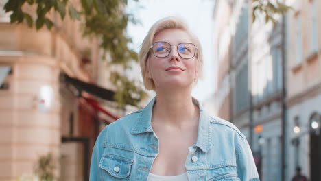 happy caucasian young woman tourist traveler in glasses looking around dreaming on city street