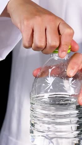 a scientist in a lab coat opens a water bottle, preparing for a chemical experiment with a beaker