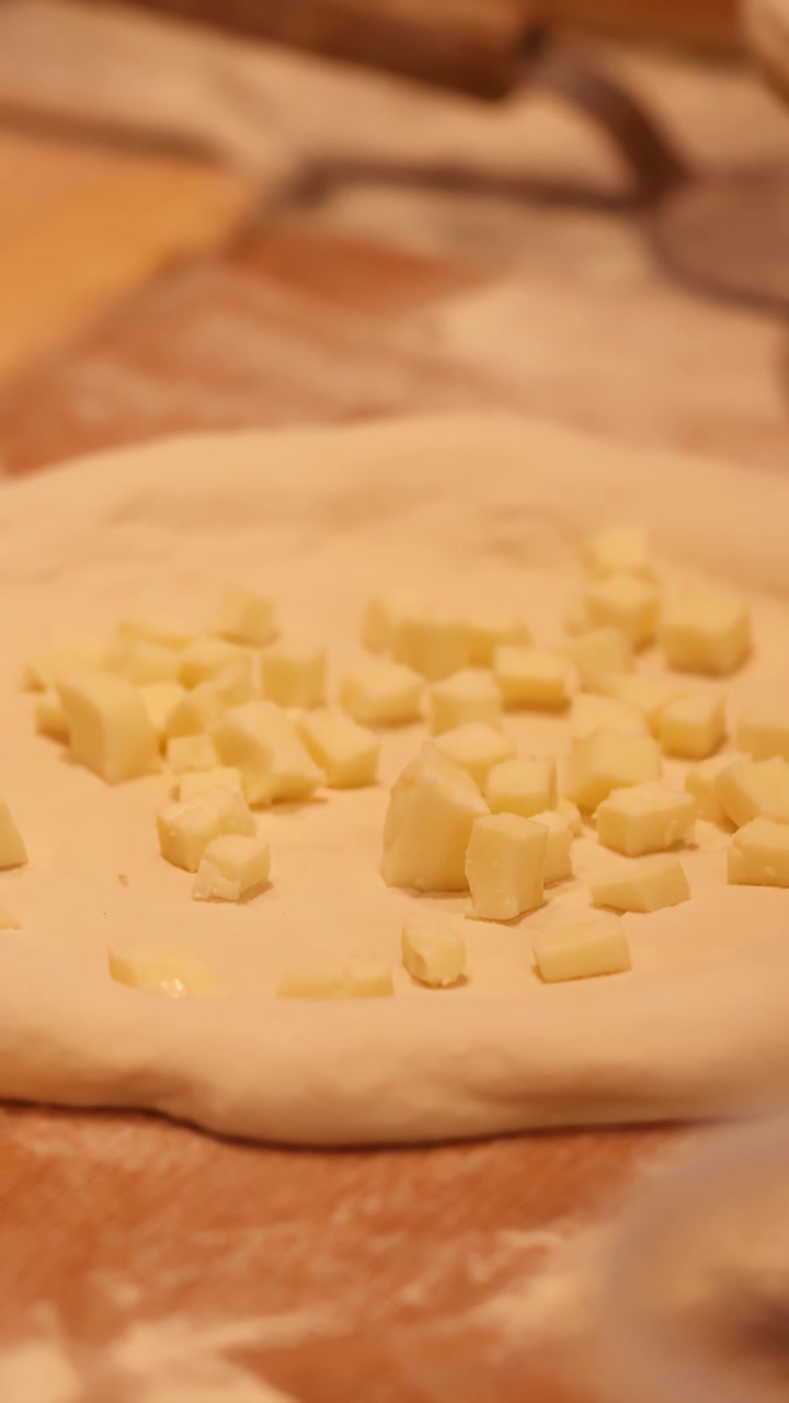 Primo piano delle mani dello chef con guanti neri che posizionano cubetti di mozzarella sull'impasto crudo della pizza.