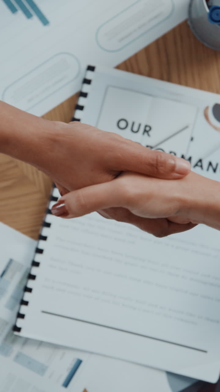 Two Business People Shaking Hands Over Performance Report on Desk
