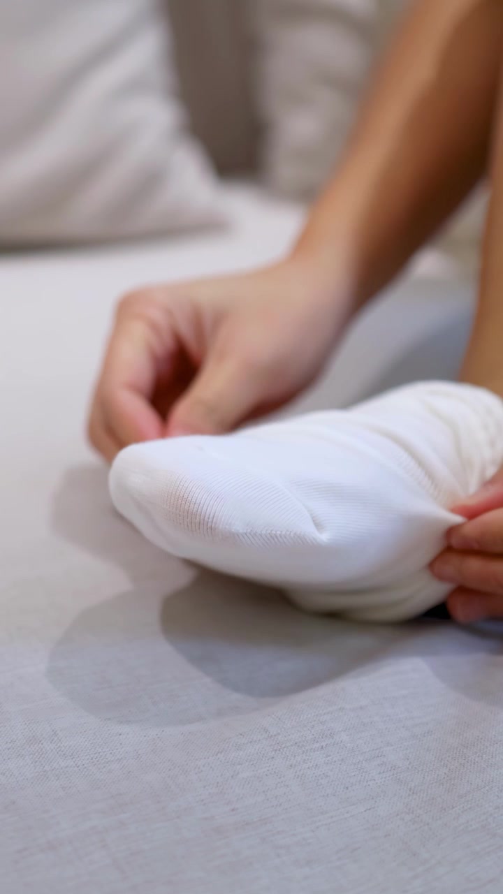 Una donna siede su un letto e indossa calzini di cotone bianchi durante la sua routine mattutina.