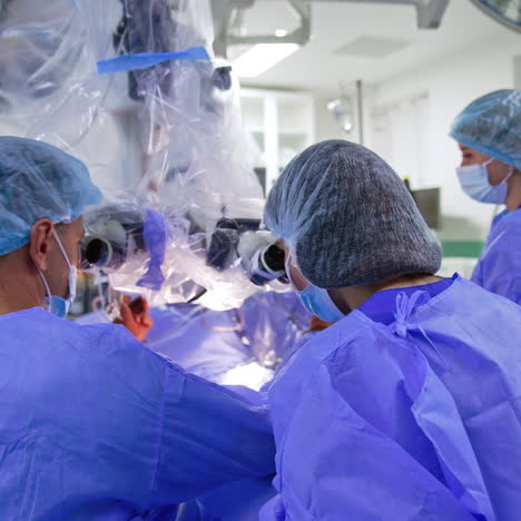 two collaborating neurosurgeons sit in front of microscope. rear view of the medics performing neurosurgery.
