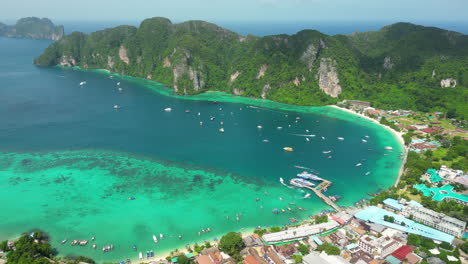 A-phenomenal-aerial-shot-of-Pi-Ley-Bay:-countless-boats-are-moored-near-the-shore,-where-a-rural-village-is-located-below-the-mountains,-Thailand