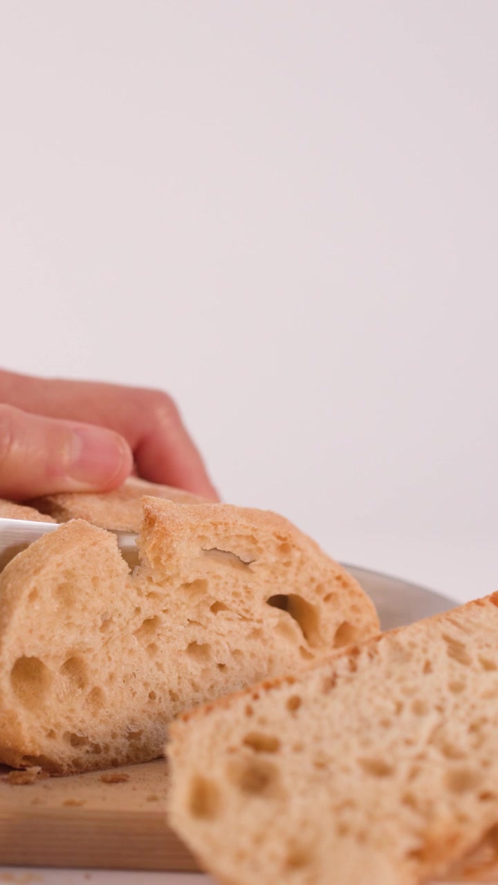 Primer plano de un chef rebanando pan de masa madre crujiente con un cuchillo sobre madera.
