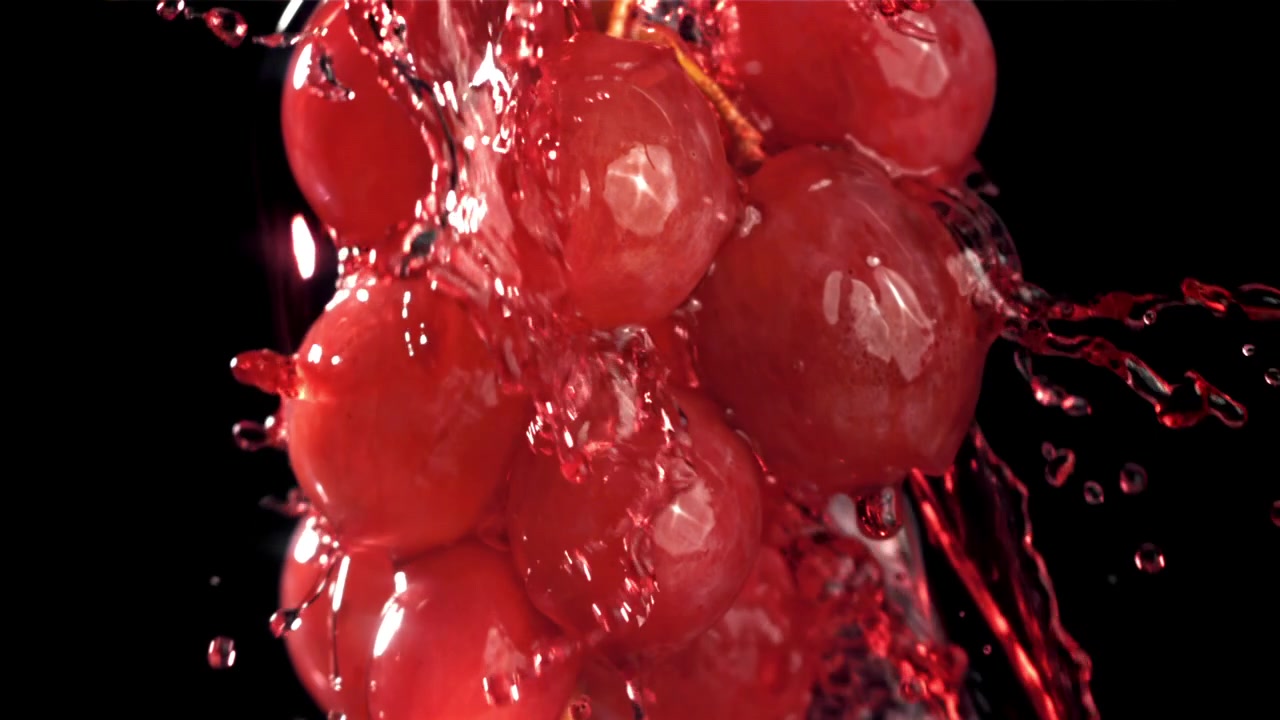 Liquido rosso che schizza su uva fresca al rallentatore.