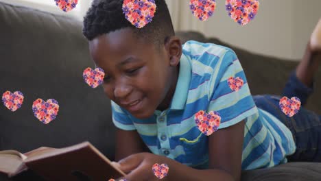 Animation-of-heart-icons-with-flowers-over-african-american-reading-reading-book