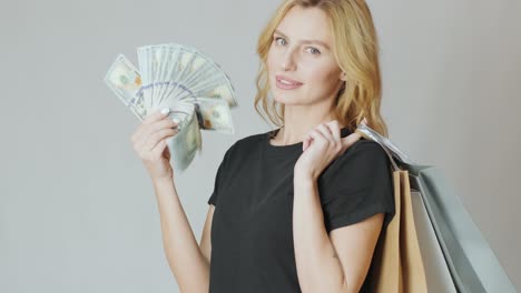 hermosa chica con un montón de dólares en las manos y bolsas de compras en el fondo blanco