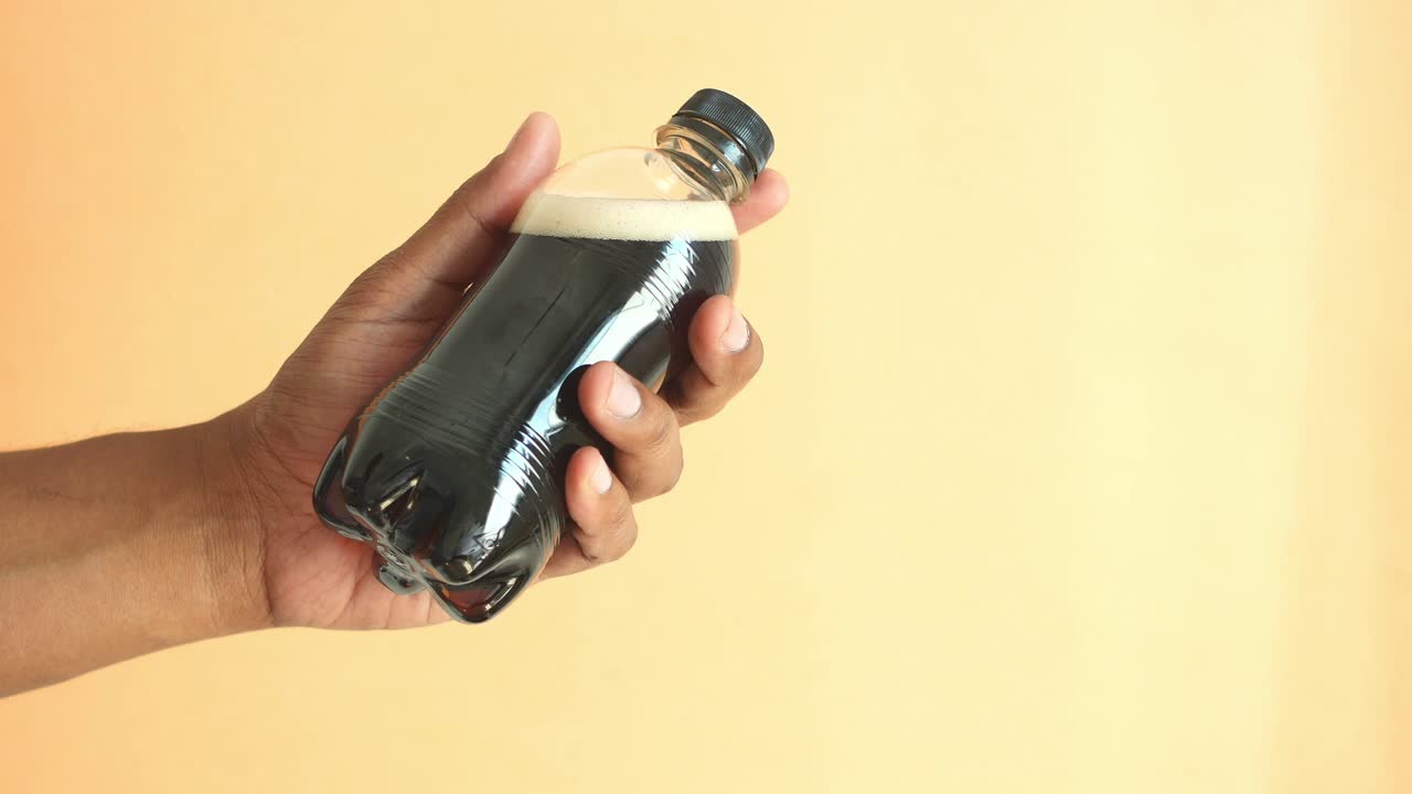 mano con una botella de refresco oscuro