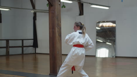 tracking shot of focused girl in kimono practicing karate in gym