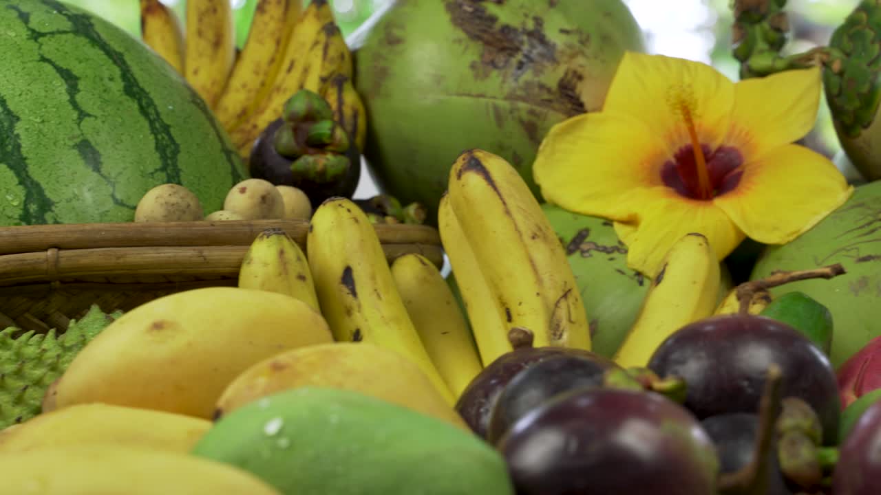 This captivating image showcases an assortment of tropical fruits commonly found in Asia, beautifully arranged with a vibrant hibiscus flower as a centerpiece.