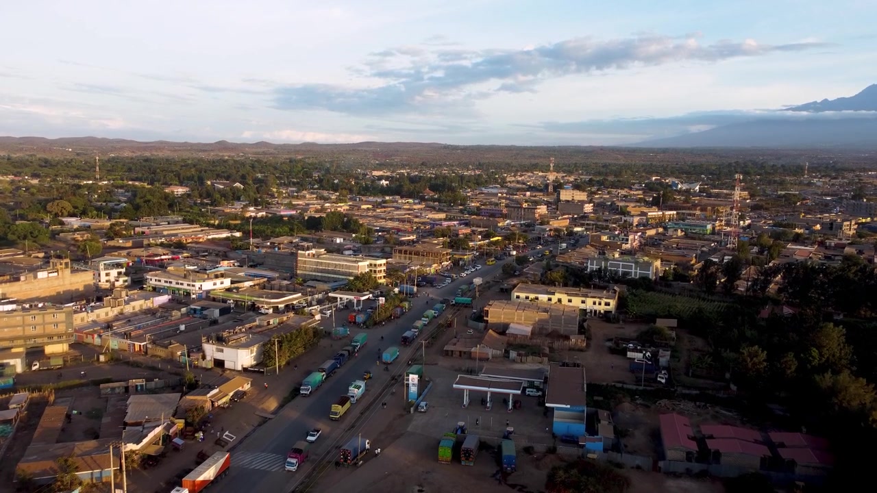 Filmiske droneoptagelser af Kimana by, der gløder i aftenlyset, med de sneklædte tinder af Kilimanjaro-bjerget, der rejser sig i baggrunden. Den travle portby ligger nær Amboseli Nationalpark.