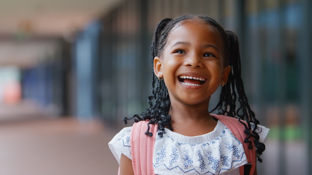 retrato de una alumna de escuela primaria sonriente al aire libre con una mochila en la escuela