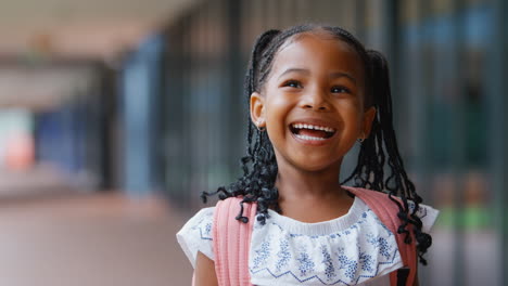 Portrait-Of-Smiling-Female-Elementary-School-Pupil-Outdoors-With-Backpack-At-School