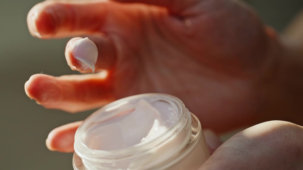 Mãos de mulher pegando creme hidratante no banheiro iniciando rotina de cuidados com a pele em close-up