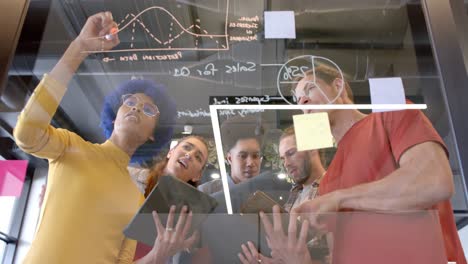 happy diverse creative colleagues brainstorming making notes on glass wall in office, slow motion