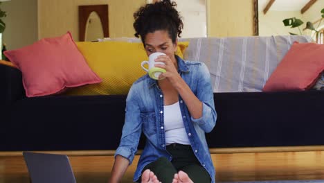 caucasian woman sitting on floor using laptop, drinking coffee, working from home