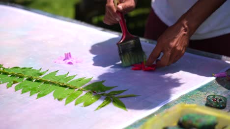 teaching-homemade-batik,-sarong,-pareo,-Dark-skin-man-wetting-hibiscus-flower-on-white-cloth,-Mahe-Seychelles-25fps-2