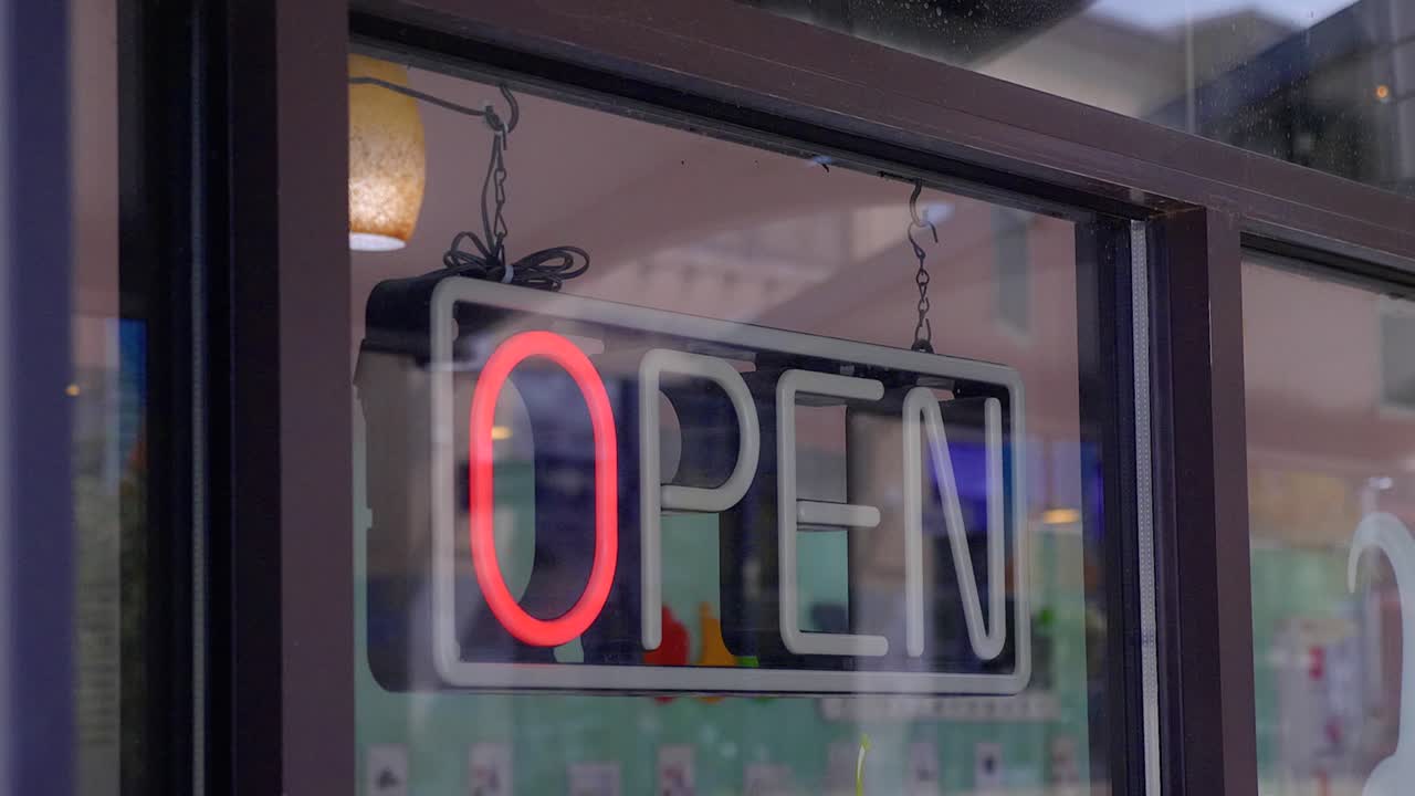 un letrero de neón abierto que parpadea a través de diferentes modos en la ventana delantera de una tienda