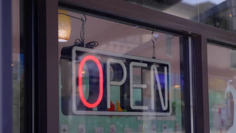 Un-Letrero-De-Neón-Abierto-Que-Parpadea-A-Través-De-Diferentes-Modos-En-La-Ventana-Delantera-De-Una-Tienda