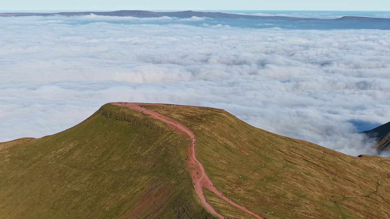 Panning telephoto aerial shot of hikers on Pen-y-Fan summit above a temperature inversion