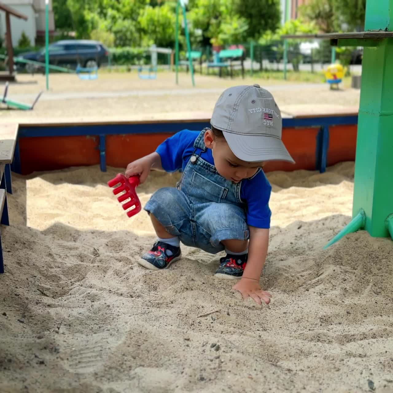 Caucasian boy deepen one hand in the sand in the sandbox. Kid rakes the sand with another hand. Playground backdrop