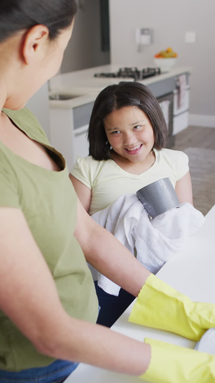 video vertical de una madre y una hija bi-raciales felices limpiando la cocina