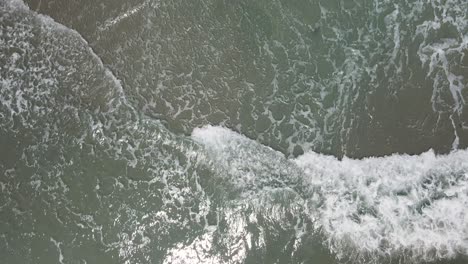 Overhead-tilting-shot-waves-crashing-along-shoreline