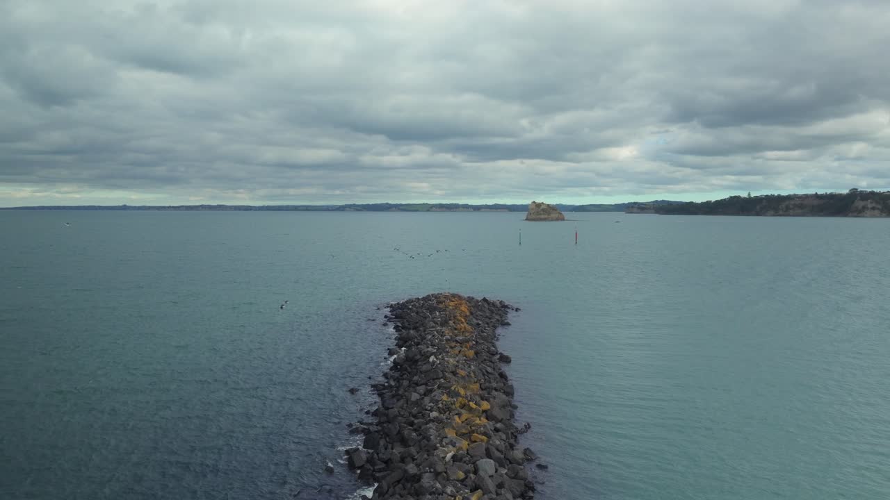 Jepretan drone udara yang terbang di atas bebatuan pesisir dengan burung-burung bergerak, dekat marina Gulf Harbour. Sebuah adegan sinematik dan damai