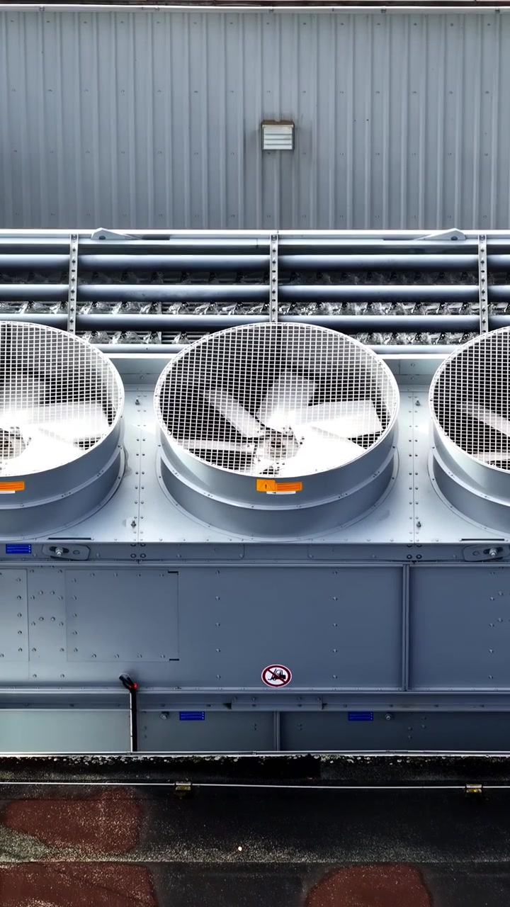 Large cooling fans operate on the rooftop of an industrial building. Useful for illustrating HVAC systems or industrial settings.