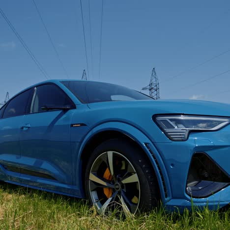 New model of audi e-tron car outdoors. Luxury electric car on the background of high voltage towers. Blue sportive model of e-tron auto for clean environment