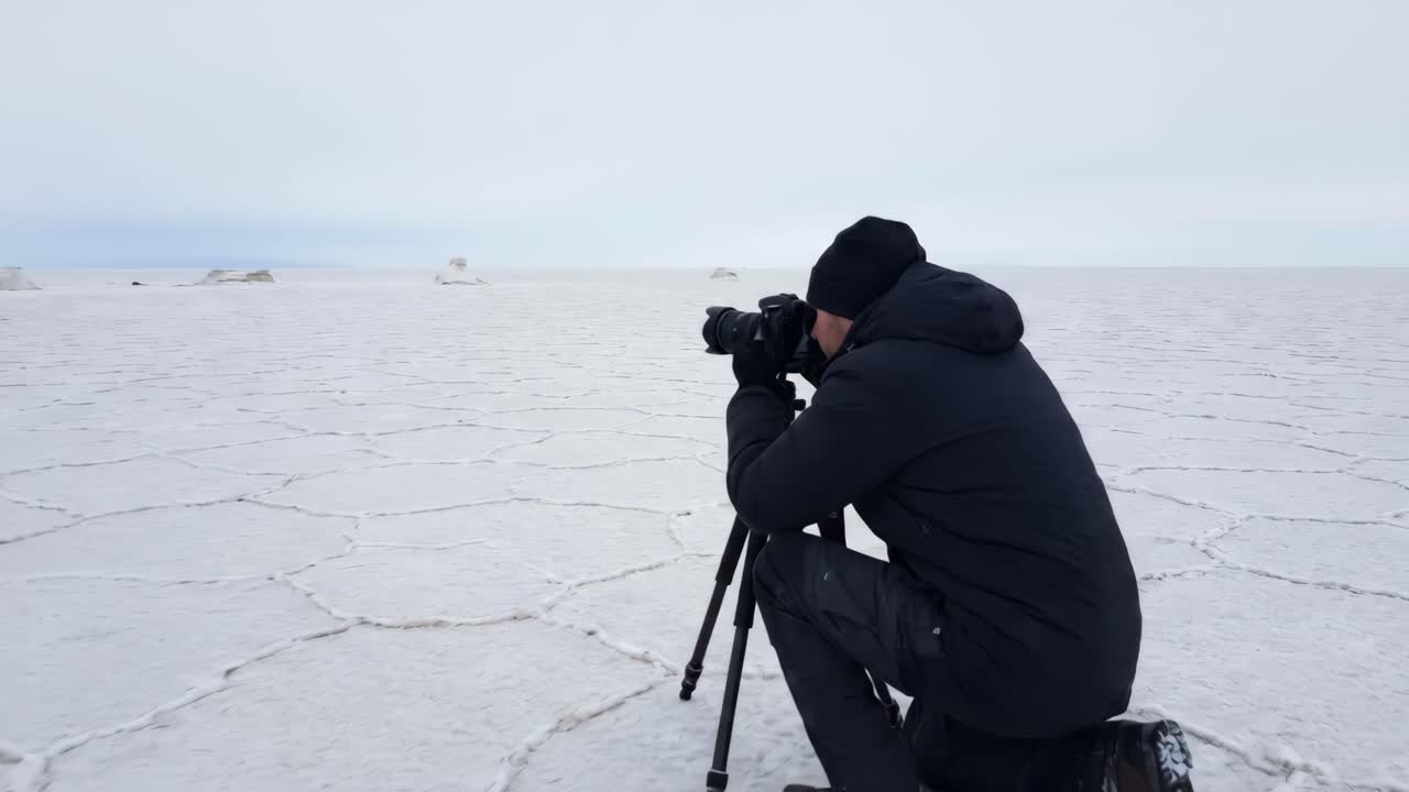 Homem fotografando uma vasta paisagem de salar branco com uma câmera em um tripé