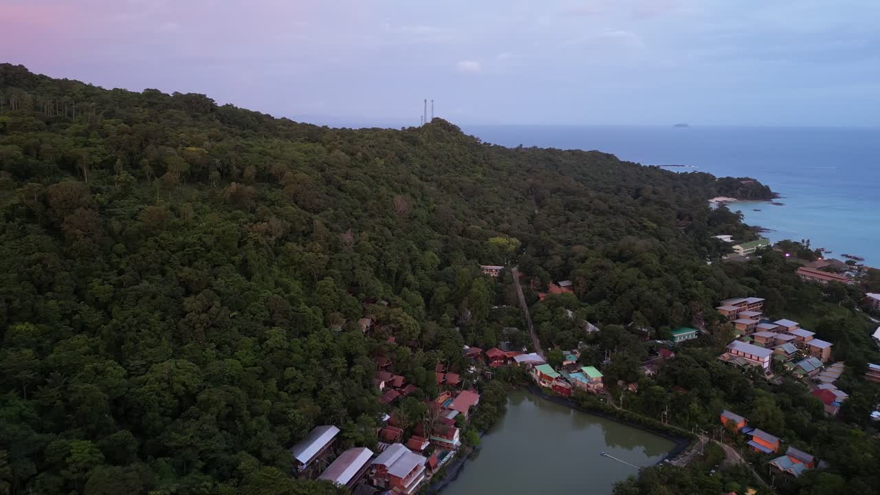 A graceful drone dolly above the lush forest of Koh Phi Phi, Thailand, glowing softly in the light of sunset.