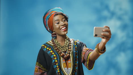 african american young beautiful woman in traditional clothes and turban making a selfie with smartphone