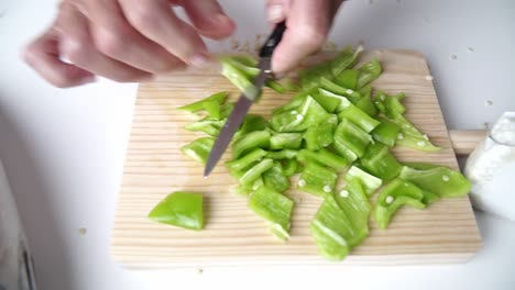 caucasian person with old hands cut green pepper on a wooden board, fish on one side of the plane