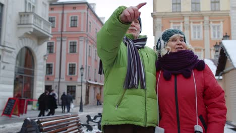 Senior-old-couple-tourists-man-woman-walking,-talking,-gesturing-in-winter-snowy-city-Lviv,-Ukraine