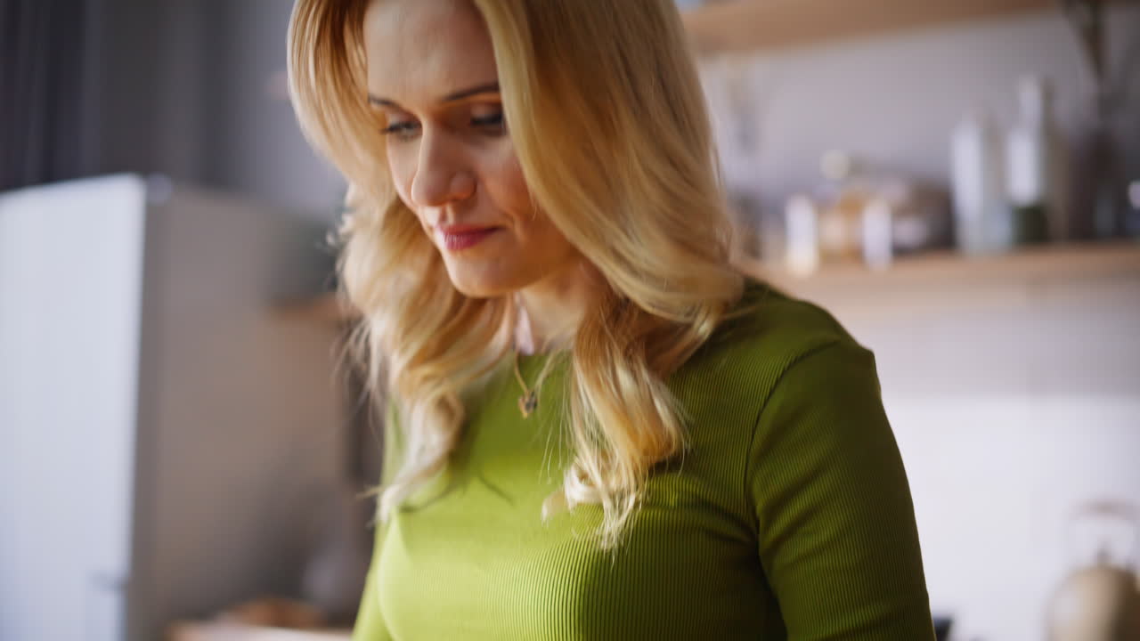 Donna che taglia le verdure in cucina mentre guarda un video culinario online, primo piano.