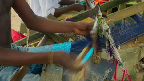 ghanaian man making kente handwoven cloth with looms rustic equipment