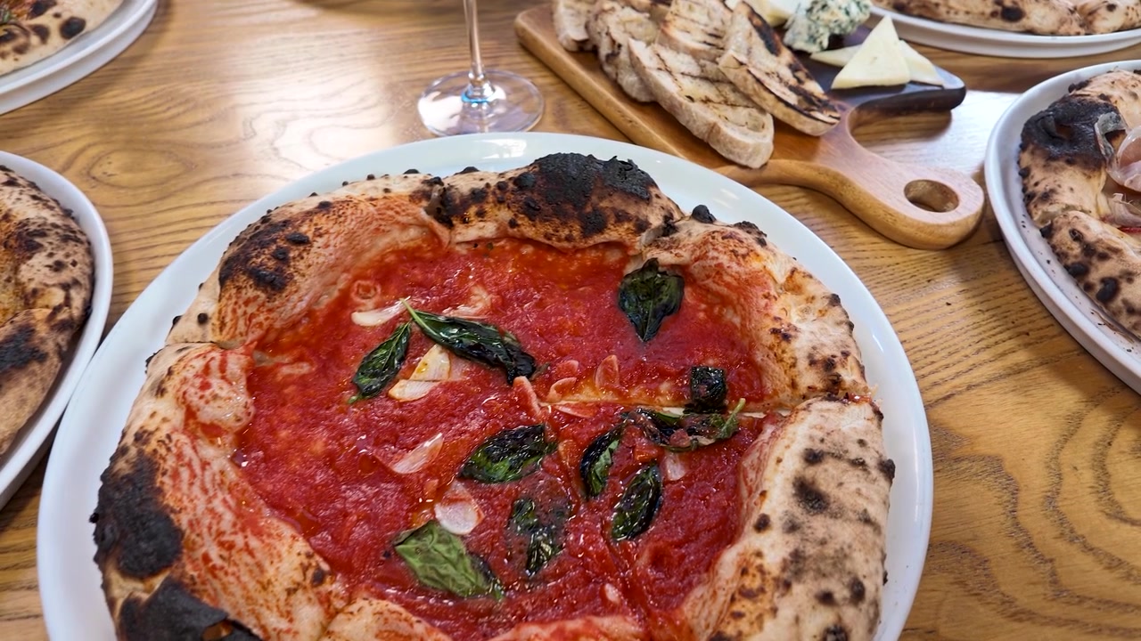 Flat lay-bild av färsk pizza, rött vin och ostbricka på restaurangbord.