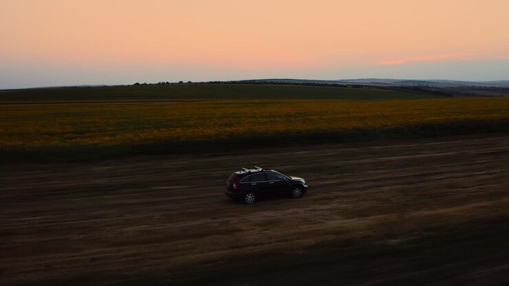 SUV off-roading near sunflower fields in the evening, drone tracking car