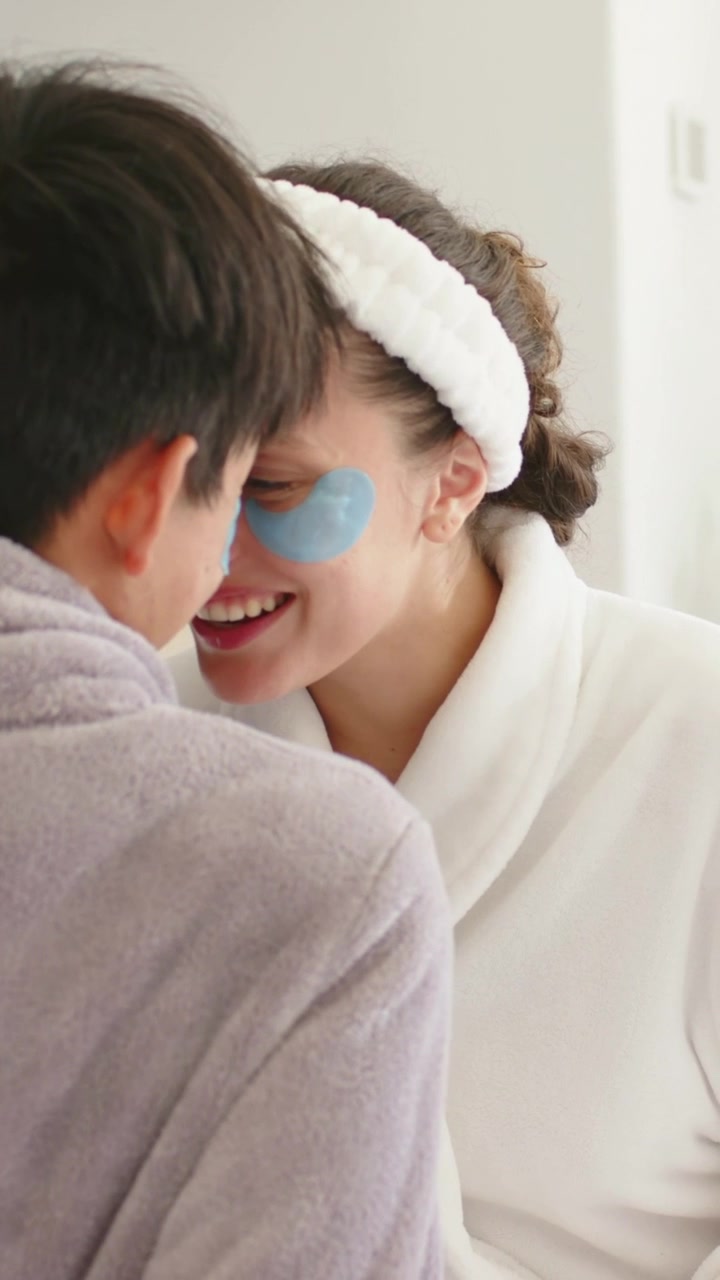 Vertical video: Smiling lady with patch in robe leaning into man touching faces at home for care