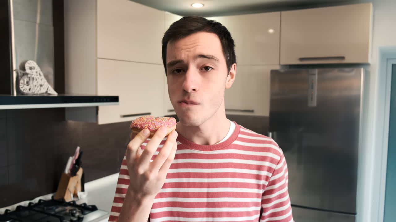 A man eating a rose donut on the kitchen and looking on it