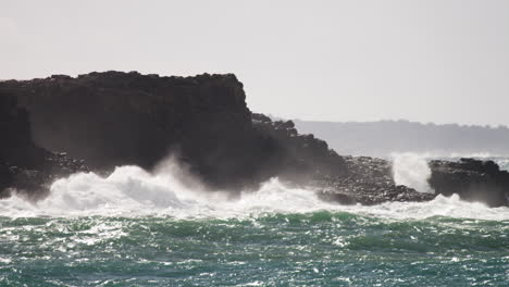 stormy waves wash around the rocks as the sun glistens on the water surface