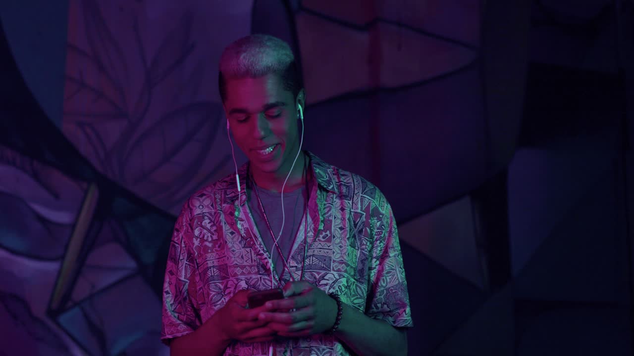tenåring afroamerikansk gutt med hodetelefoner mens du lytter til musikk og tekst på telefonen ute om natten